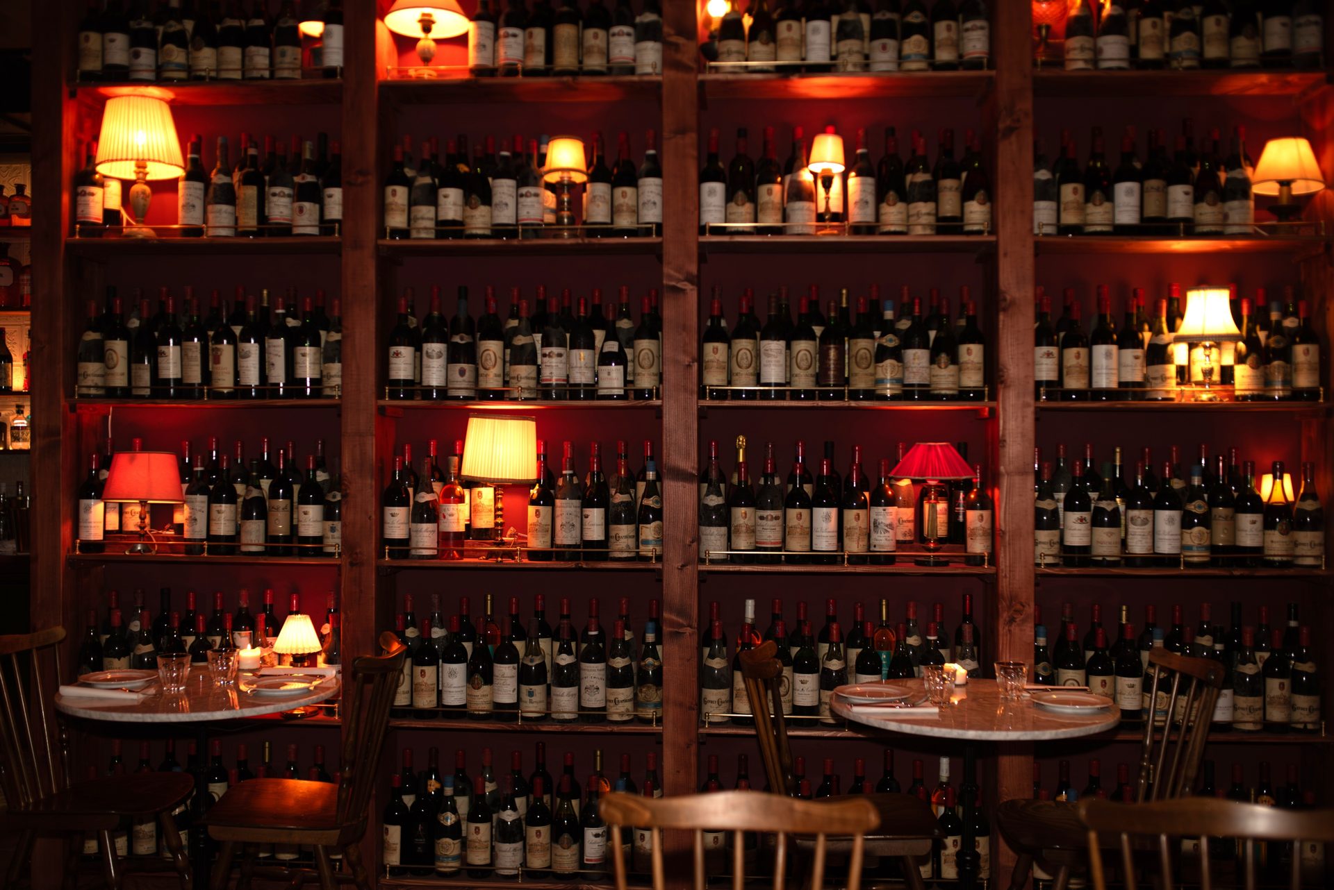 The dining room of Lupaia Osteria in Lausanne, with its shelves of wine bottles, small lamps and laid tables