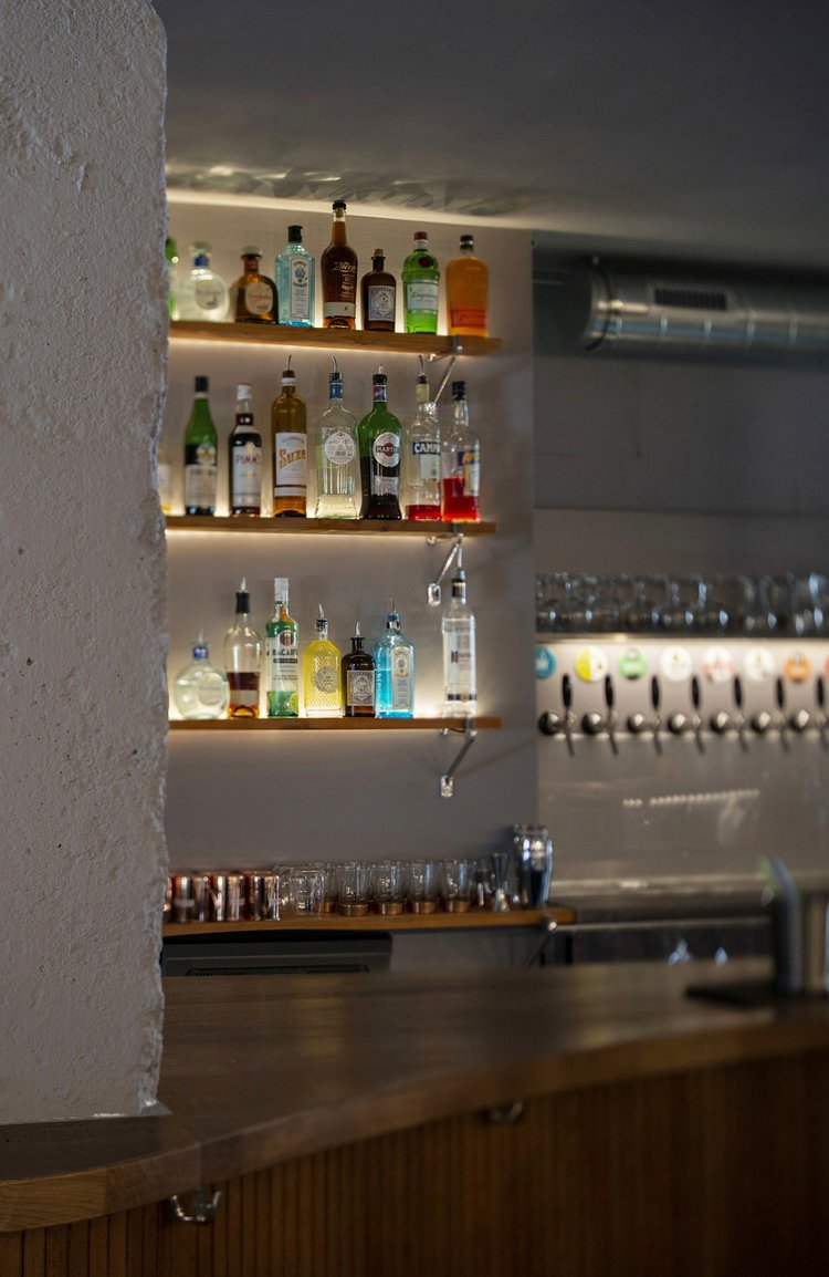 The bar counter at Café du Simplon with lit bottle shelving and beer taps