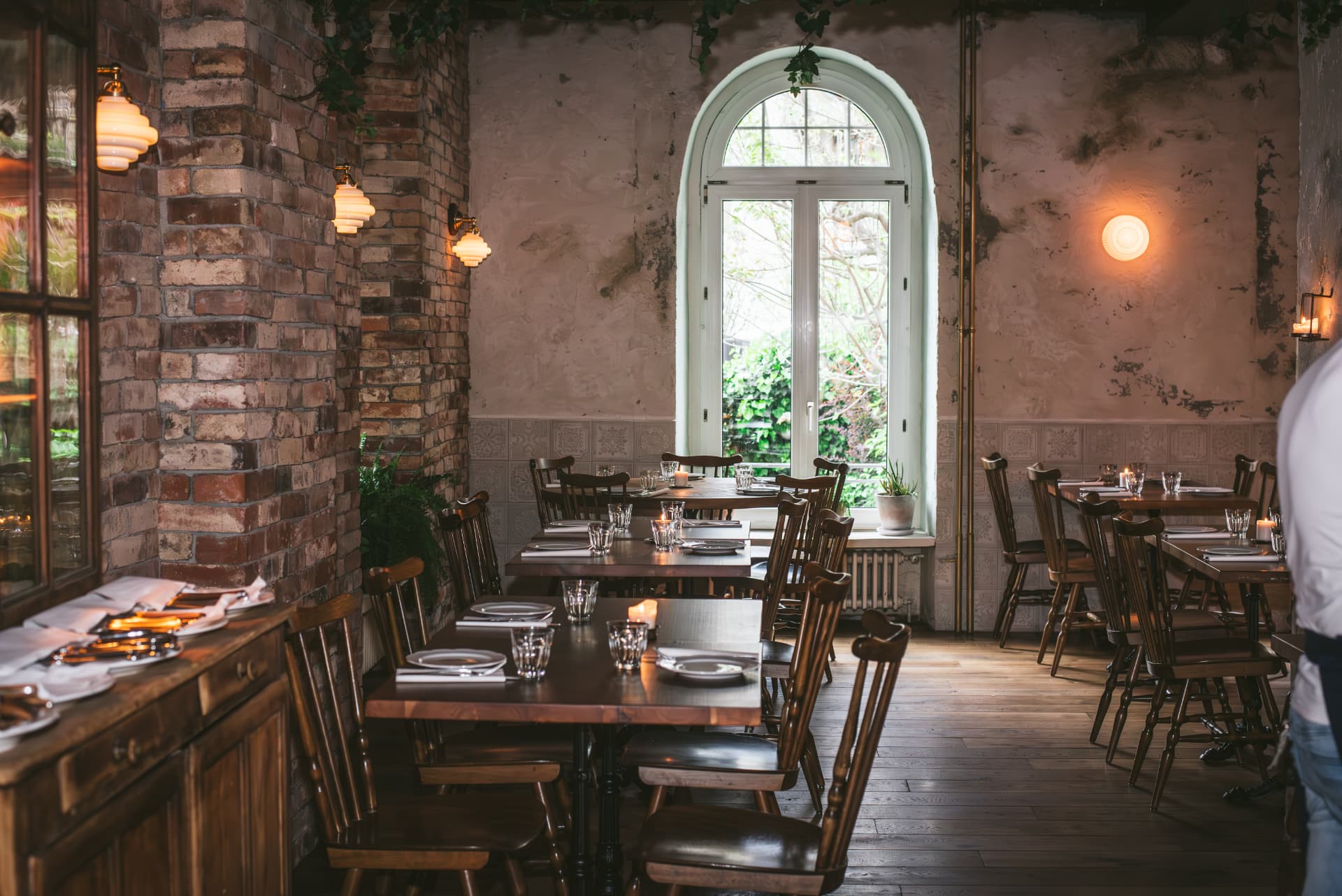 The indoor dining room of Lupaia Osteria, brick walls, tall windows and laid tables