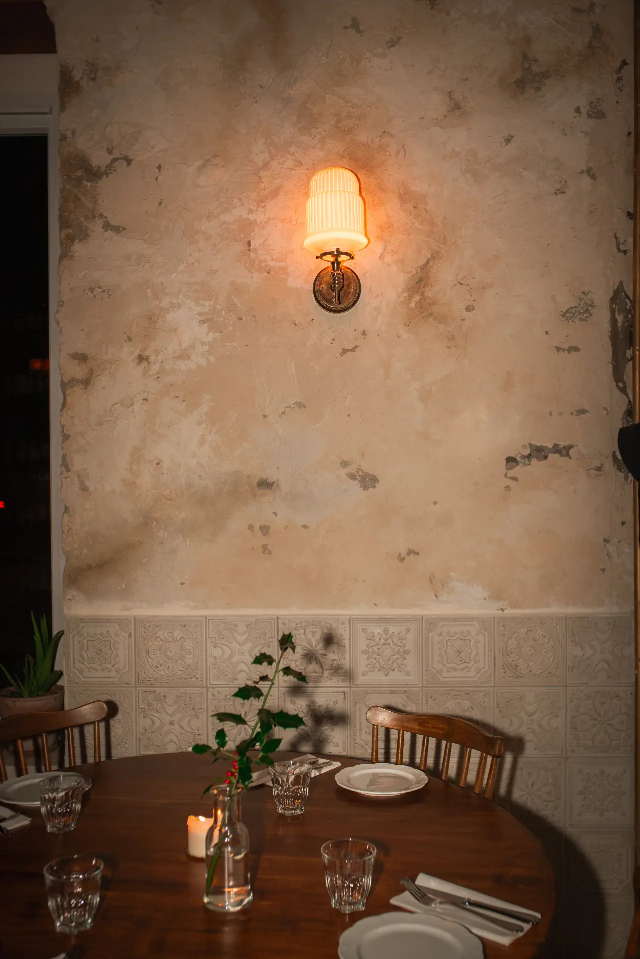 A round table laid at Lupaia Osteria beneath a wall light, against weathered plaster