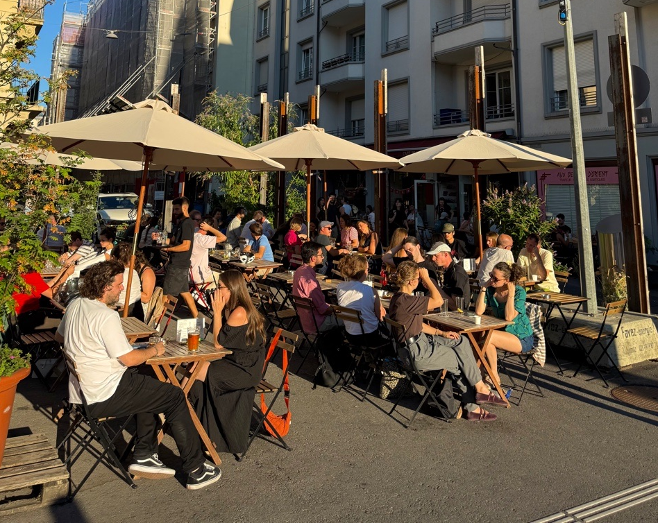 The busy large terrace at Café du Simplon, with parasols and guests seated in the sun